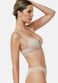 Kant bralette en bijpassende slip in nude. Heeft textuur met bloemmotieven, dunne bandjes en subtiele gouden accenten. Glad afwerking.