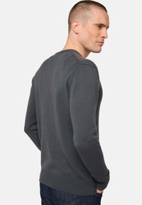 Pull en maille gris avec un col rond, des poignets et un ourlet côtelés, au design ajusté, présentant un tissu texturé et une couleur unie.