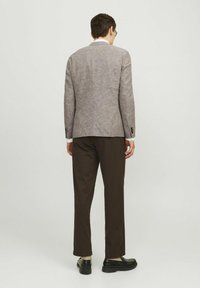 Blazer texturizado de color marrón claro con corte ajustado, botones negros y detalles de costura, combinado con pantalones marrón oscuro y zapatos negros.