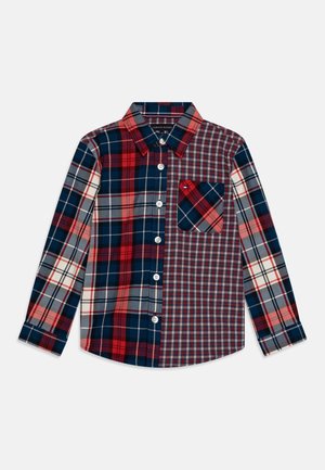 Chemise à manches longues à boutons avec des motifs de tartan mélangés en rouge, marine et gris, présentant une poche poitrine avec un design de tartan diagonal.