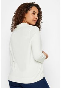 Suéter blanco de punto con un cuello alto, mangas tres cuartos y un corte relajado, detallado con dobladillo acanalado y aberturas laterales.