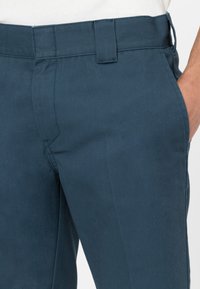 Pantaloni blu scuro realizzati in tessuto morbido, con frontale piatto, passanti per cintura e tasche laterali. Taglio pulito con dettagli di cucitura sottili.