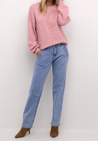 Rosa gestrickter Pullover mit Blumenstickerei, kombiniert mit hellblauen Denim-Jeans mit geradem Bein und braunen Stiefeletten mit Absatz.