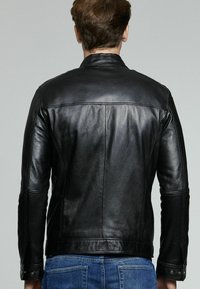 Chaqueta de cuero negro con una textura suave, diseño ajustado y detalles de costura mínimos. Presenta un cuello alto y acentos de metal.