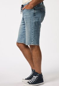 Shorts de mezclilla en azul claro, con una cintura elástica y cordón, bolsillos laterales y un corte recto. Combinados con zapatillas altas en azul marino.