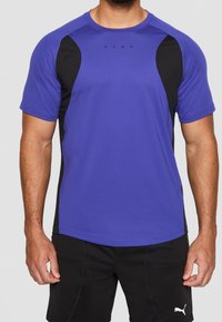 Camiseta atlética morada con paneles laterales negros, mangas cortas, cuello redondo y logo de Puma en el pecho. Tejido ligero y transpirable.