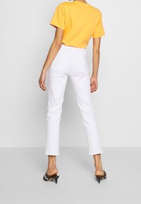 Camisa amarilla de manga corta combinada con pantalones blancos de talle alto. Los pantalones tienen pernera recta y bolsillos traseros, lo que revela un diseño elegante.