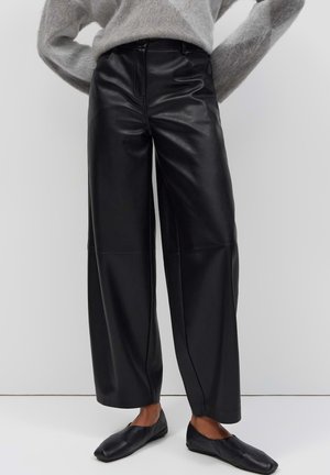 Persona che indossa pantaloni in pelle neri a vita alta e a gamba larga abbinati a scarpe basse nere e a un maglione grigio morbido a maniche lunghe.