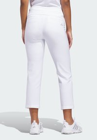 Λευκά κάπρι παντελόνια με λεία υφή, διαθέτουν ψηλή μέση, πίσω τσέπες και διακριτική λεπτομέρεια λογότυπου. Φοριούνται με λευκά αθλητικά παπούτσια.