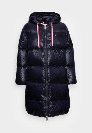 Long navy blue puffer coat with hood, front zipper, and white-red-striped drawstrings on the hood, quilted horizontal sections.