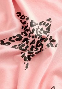 Vaaleanpunainen kangas, jossa on musta leoparditulkinta tähti kuvio, jolla on sileä pinta, esittäen poimuja ja ryppyjä.