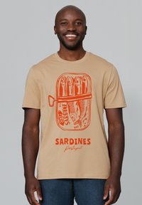 Beige T-Shirt mit einem grauen Fischerboot, das in der Mitte des Shirts abgebildet ist. Darunter sind Fische und das Wort "SARDINES Portugal" auffällig dargestellt.
