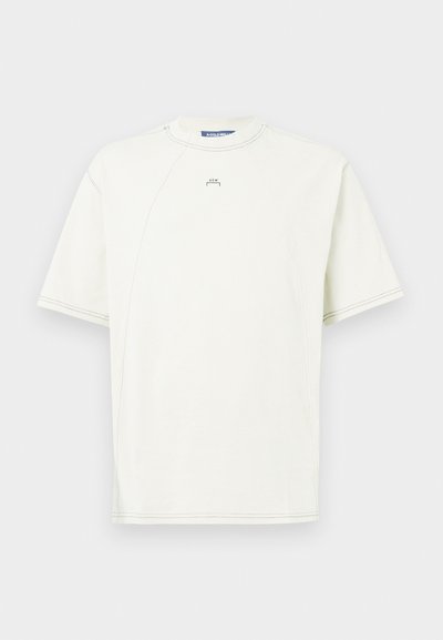 Tricou scurt din bumbac, de culoare crem deschis, cu mâneci raglan, decolteu circular și detalii minime de cusătură. Logo mic pe față.