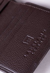 Brown leather cardholder with a textured finish, featuring four card slots and embossed logo, against a light background.