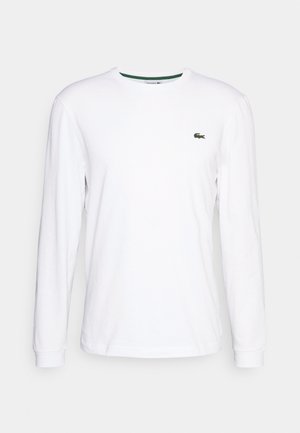 T-shirt bianca a maniche lunghe in cotone con scollatura rotonda e logo ricamato verde sul lato sinistro del petto. Tessuto morbido e design aderente.