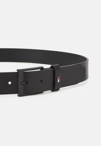 Cintura in pelle nera con fibbia rettangolare opaca nera e piccolo logo quadrato rosso, bianco e nero sul passante in pelle.