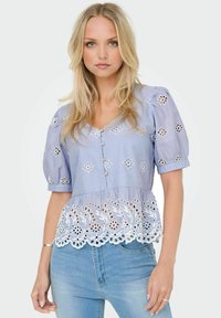 Blouse bleu clair avec des manches bouffantes et un devant à boutons, ornée de broderies florales et de dentelle le long de l'ourlet. Tissu en coton texturé.