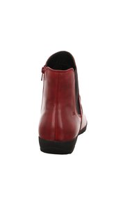 Bottine en cuir rouge avec une finition lisse, des panneaux élastiques sur les côtés et une fermeture éclair à l'arrière. La semelle en caoutchouc noir offre une bonne adhérence.