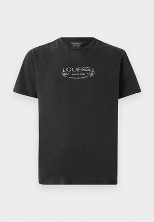 Čierne tričko s krátkym rukávom s potlačou textu "GUESS Since 1981 Authentic Design" a dekoratívnymi prvkami na hrudi.