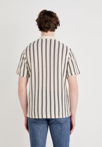 Koszula krótki rękaw w paski w kolorze kremowym i czarnym. Charakteryzuje się tkanym teksturą z pionowymi paskami oraz miękkim kołnierzykiem. Widok z tyłu ukazuje luźny krój.