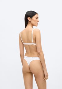 Biele bavlnené spodné prádlo s jednoduchým dizajnom, tenkými nastaviteľnými ramienkami a pásom s logom "TOMMY HILFIGER" v kontrastnej farbe.