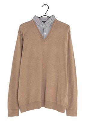 Pull marron col en V superposé sur une chemise à carreaux noirs et blancs, sur un cintre noir.
