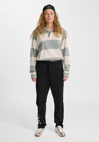 Langemouwen gestreepte polo in groen en room met een logo, gecombineerd met zwarte joggingsbroek met een trekkoord en zijaccenten.