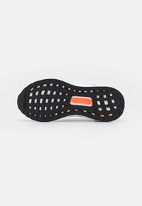Semelle de chaussure en caoutchouc noir avec un motif texturé, dotée d'accents blancs et orange, conçue pour l'adhérence et la durabilité.