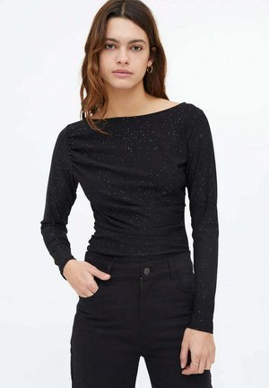 Top negro de manga larga con escote barco, con manchas metálicas por toda la prenda y un diseño ajustado. Combinado con pantalones negros.