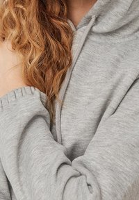Sudadera gris claro con una tela suave y texturizada. Cuenta con un bolsillo en la parte frontal y puños fruncidos para un ajuste relajado. Diseño con capucha.