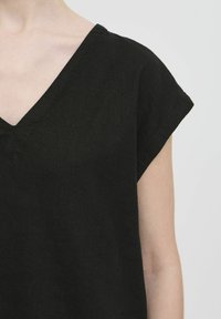 Top nero a scollo a V con maniche corte arrotolate. Realizzato in un tessuto testurizzato, ha una vestibilità ampia e dettagli di cucitura minimi.