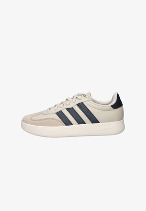 Beige Adidas sneaker with black three stripes, lace-up closure, cushioned sole, and black heel tab, shown in side profile.