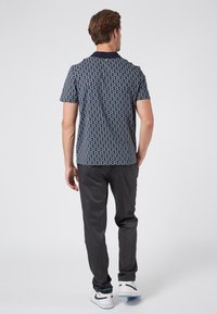 Kortärmad skjorta i marinblått med geometriskt mönster; kombinerad med mörka slim-fit byxor och vita sneakers, med en smidig yta.