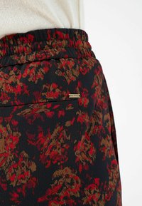 Schwarzer Rock mit Blumendesign in Rot- und Brauntönen, mit einem elastischen Taillenbund und einem kleinen Markenetikett an der Tasche.