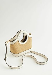 Petit sac à main en paille tressée avec garniture en cuir blanc, poignées rondes découpées et longue bandoulière amovible en cuir blanc.