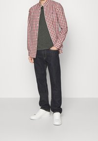 Röd och vit rutigt skjorta över en mörkgrå t-shirt, kombinerad med mörkblå jeans och vita sneakers. En enkel, avslappnad outfit.