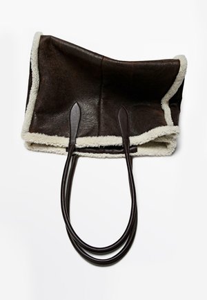 Brun lædertaske med blød hvid uldkant og to lange brune læderhåndtag, med et rummeligt, åbent design.