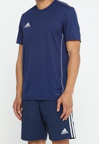 Navy atletisk tröja med korta ärmar, med vita accentlinjer och en Adidas-logotyp på bröstet. Bärs med matchande navy shorts.