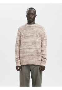 Hellrosa gestrickter Pullover mit rundem Ausschnitt und langen Ärmeln, mit einem strukturierten, gestreiften Muster. Kombiniert mit grauen, weit geschnittenen Hosen.