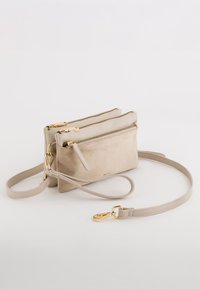 Beige Leder Umhängetasche mit zwei Rei�ßverschlusstaschen, schlankem Design, goldfarbenen Beschlägen und einem verstellbaren Gurt.
