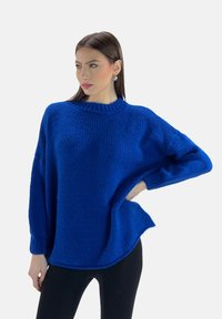 Maglione oversize, blu, lavorato a maglia con collo alto, maniche morbide e orlo arrotondato. Il materiale sembra elastico e spesso.