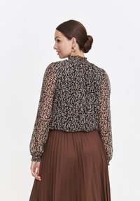 Czarna bluzka w kwiaty z długimi, przezroczystymi rękawami; posiada wysoki dekolt i detal w postaci łezki z tyłu. Połączona z brązową spódnicą z plisami.