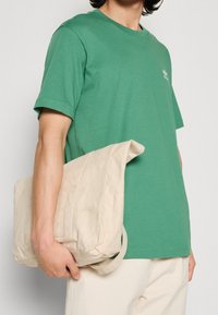 Grön bomulls-t-shirt med korta ärmar, kombinerad med en beige canvasväska med en enkel design och axelrem.