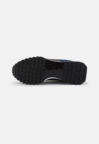 Sole di scarpa sportiva nera in gomma texturizzata, con scanalature per la trazione e un design elegante. Accentuata da una striscia riflettente.