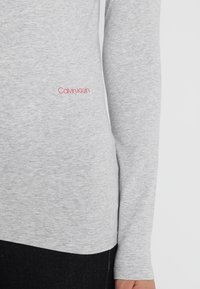 Graues Langarmhemd aus weichem Baumwollmix. Verfügt über ein rotes "Calvin Klein"-Logo auf der unteren linken Seite. Slim-Fit-Design.
