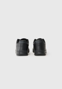 Baskets en cuir noir avec une forme arrondie, une finition texturée et une semelle en caoutchouc. Présente un logo ton sur ton sur le talon.