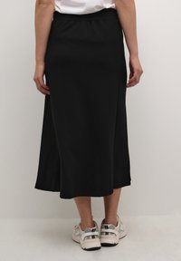 Musta midi-hame, jossa on sileä pinta, joustava vyötärö ja kevyet levennykset helman kohdalla. Yhdistetty vaaleanvärisiin urheilukenkiin.