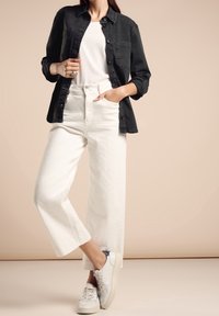 Svart denimskjorta lager på en vit t-shirt, kombinerad med högmidjade vita byxor med vida ben och vita sneakers med marinblå detaljer.