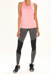 Różowy sportowy top na ramiączkach i szare legginsy z czarnymi siateczkowymi akcentami. Top ma dopasowany krój; legginsy przylegają do ciała z efektownym kontrastem kolorystycznym.