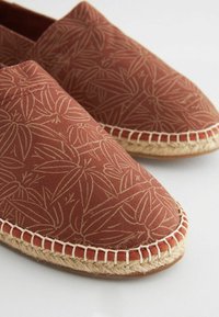 Červené kanvasové slip-on topánky s vzorom listov, jutené lano okolo podrážky a hladká textúra. Ľahký a neformálny dizajn.
